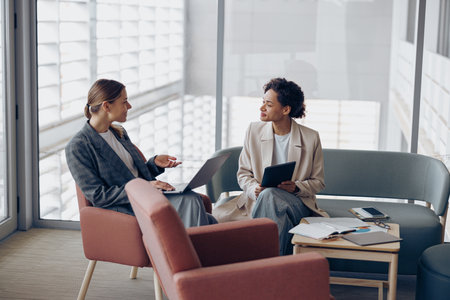 Stylish female coworkers talking during business meeting in cozy office. Teamwork conceptの写真素材