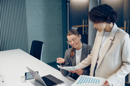 Two smiling business woman work together with documents to get the job done at the officeの写真素材