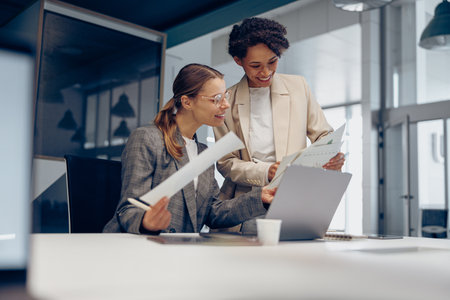 Two smiling business woman work together with documents to get the job done at the officeの写真素材