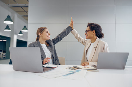Smiling stylish business people giving each other a high five while working on laptop in coworkingの写真素材