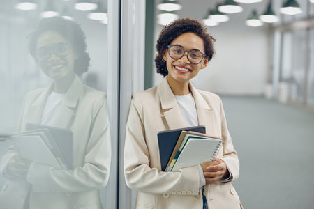 Pretty female manager in eyeglasses standing on office background and looks camera with smileの写真素材