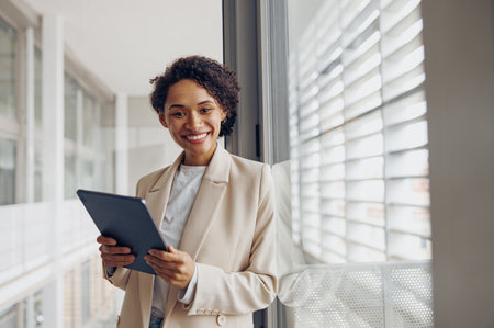 Smiling female manager with digital tablet standing on modern office background and looks cameraの写真素材