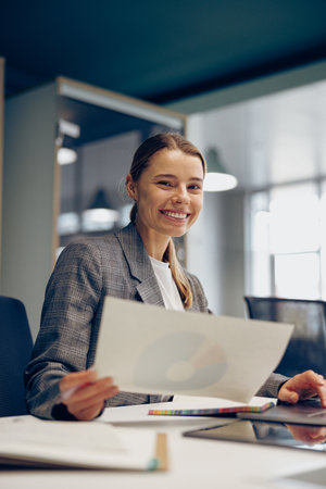 Positive female accountant working with financial statement and use laptop while sitting in officeの写真素材