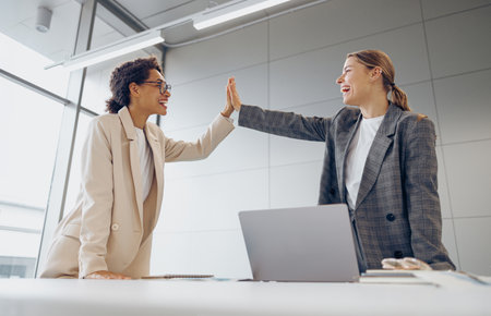 Successful business people giving each other a high five while working on laptop in coworkingの写真素材