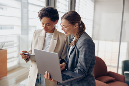 Group of female managers standing in modern office while working on laptop and digital tabletの写真素材