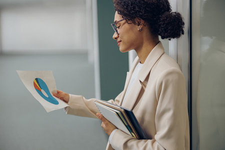 Stylish female financial analyst looking on documents while standing on office backgroundの写真素材