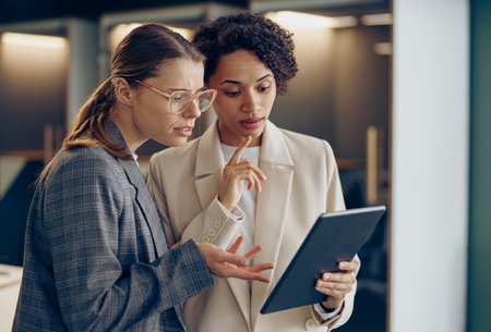 Young female sales managers standing in modern coworking and using digital tablet togetherの写真素材