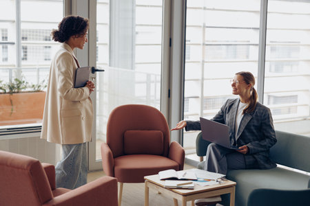 Businesswoman with laptop is sitting in office and making welcome sign to client.の写真素材