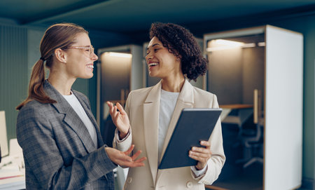 Smiling female business people standing in modern coworking and using digital tablet togetherの写真素材