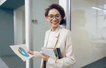Pretty female entrepreneur looking on financial documents while standing on office backgroundの写真素材