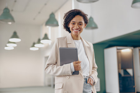 Smiling business woman with digital tablet standing on modern office background and looks cameraの写真素材