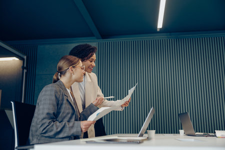 Two smiling business woman work together with documents to get the job done at the officeの写真素材
