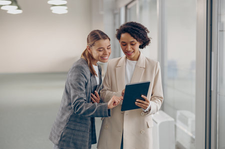 Stylish busy female coworkers discussing project standing in modern office and use digital tabletの写真素材