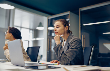 Focused business woman working on laptop while sitting the desk in office on colleague backgroundの写真素材