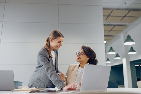 Two busy female coworkers discussing project while working in office and use laptopの写真素材