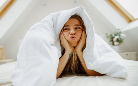 a woman is making a funny face while laying under a blanket on a bedの写真素材
