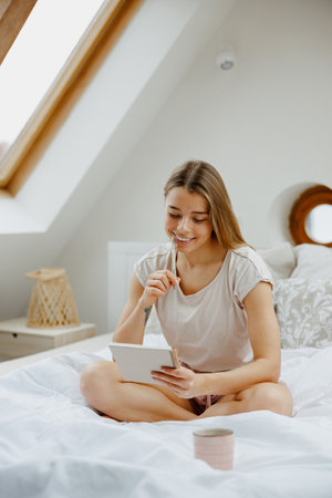 A woman is seated on a wooden bed and making notes in note padの写真素材