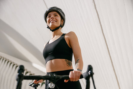 Young female cyclist in protective gear looking at camera while riding bicycle in city centerの写真素材
