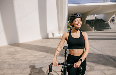 Woman cyclist in protective gear standing with her bike while training outdoors and looks awayの写真素材