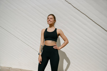 Smiling woman in sportswear have a rest after workout outside standing on building backgroundの写真素材