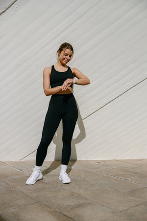 Smiling woman in sportswear looking on smartwatch after training. Outdoor sports in the morningの写真素材