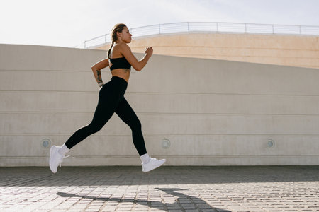 Active woman athlete is jogging in morning on modern building background. Healthy life conceptの写真素材