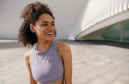 Smiling woman in tracksuit have rest after workout outside standing on building backgroundの写真素材