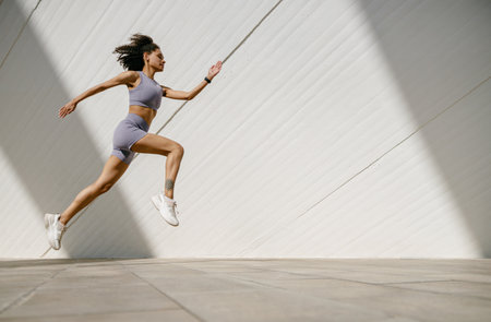 Active woman athlete is jogging in the air on modern building background. Healthy life conceptの写真素材