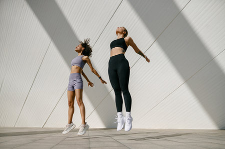 Women athlete in sportswear leaping in air with wall backdrop outdoors. Healthy lifestyle conceptの写真素材