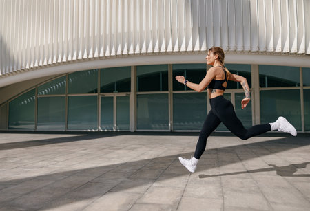 Young woman in sportswear is running on modern buildings background. Active lifestyle conceptの写真素材