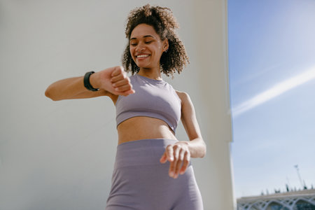 Smiling woman in sportswear looking on smartwatch after training. Outdoor sports in the morningの写真素材