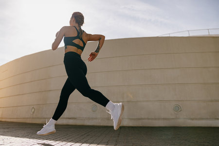 Side view of woman athlete is jogging in morning on modern building background. Healthy life conceptの写真素材