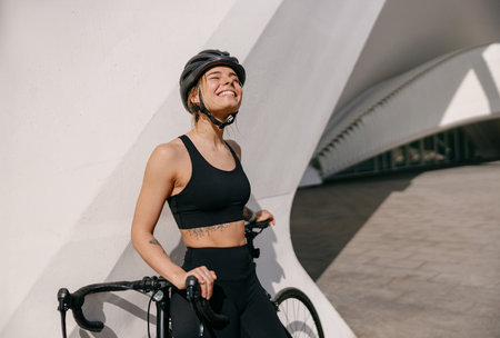 Professional female cyclist in protective gear looking at sun while riding bicycle in cityの写真素材