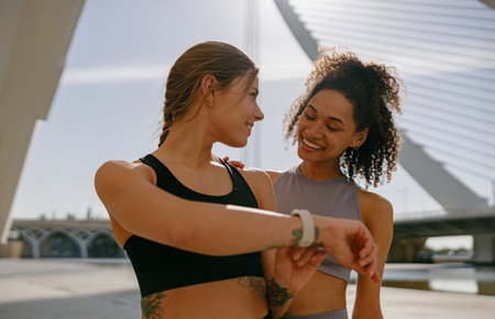 Smiling woman with female friend looking on smartwatch before exercising standing outdoorsの写真素材