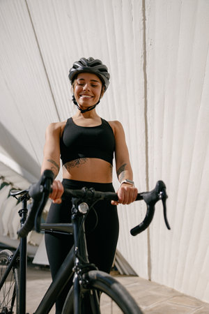 Smiling woman cyclist in protective gear standing with her bike while training outdoorsの写真素材