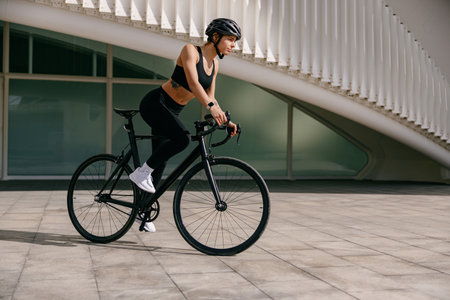 Active female cyclist in sportswear helmet cycle outdoors on city building backgroundの写真素材