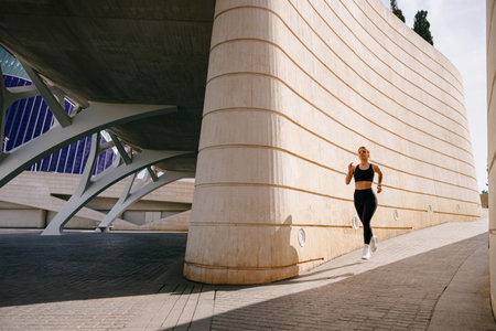 Active woman athlete is jogging in morning on modern building background. Healthy life conceptの写真素材