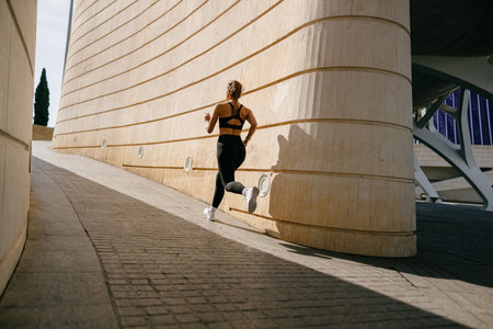 Back view of woman athlete in sportswear is running on buildings background. Active lifestyle conceptの写真素材