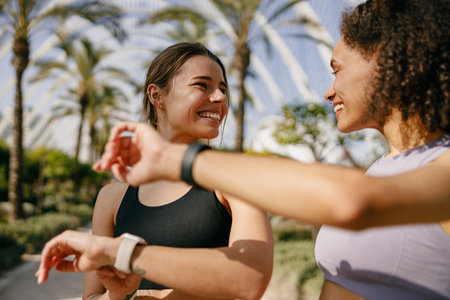 Smiling woman with female friend looking on smartwatch before exercising standing outdoorsの写真素材