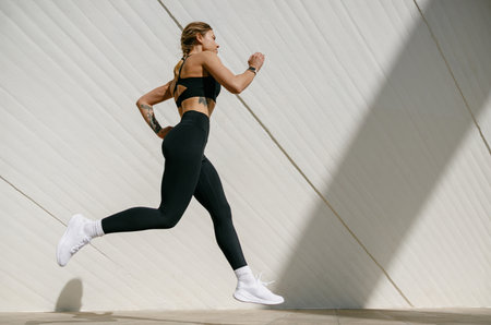 Active woman athlete is jogging in morning on modern building background. Healthy life conceptの写真素材