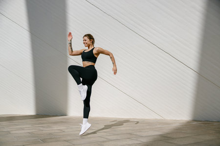Female athlete in sportswear leaping in air with wall backdrop outdoors. Healthy lifestyle conceptの写真素材