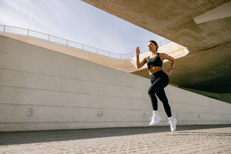 Young woman in sportswear is running on modern buildings background. Active lifestyle conceptの写真素材