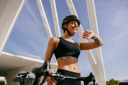 Female cyclist in helmet looking at smartwatch and counting calories burned. Healthy life conceptの写真素材