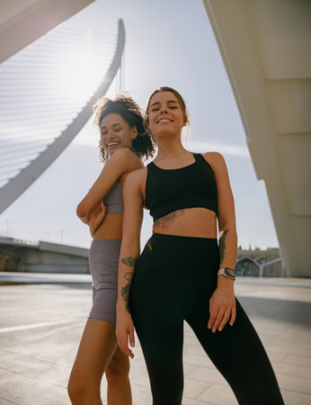 Two young female sportswomen have a rest after morning jogging standing outdoors and looks cameraの写真素材