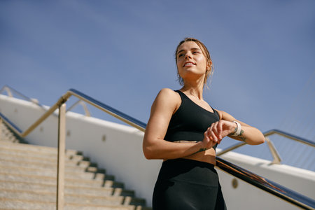 Smiling woman in sportswear looking on smartwatch after training. Outdoor sports in the morningの写真素材