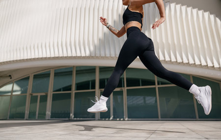 Close up of woman athlete is jogging in the air on modern building background. Healthy life conceptの写真素材
