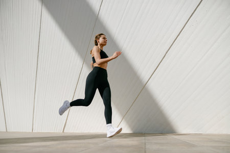 Active woman athlete is jogging on morning on modern building background. Healthy life concept