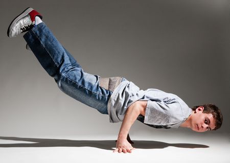 breakdancer balancing on his hands against grey background