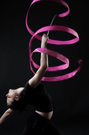 beautiful gymnast with pink ribbon against dark backgroundの写真素材