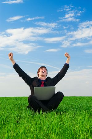 happy businessman with laptop sitting at the grassの写真素材